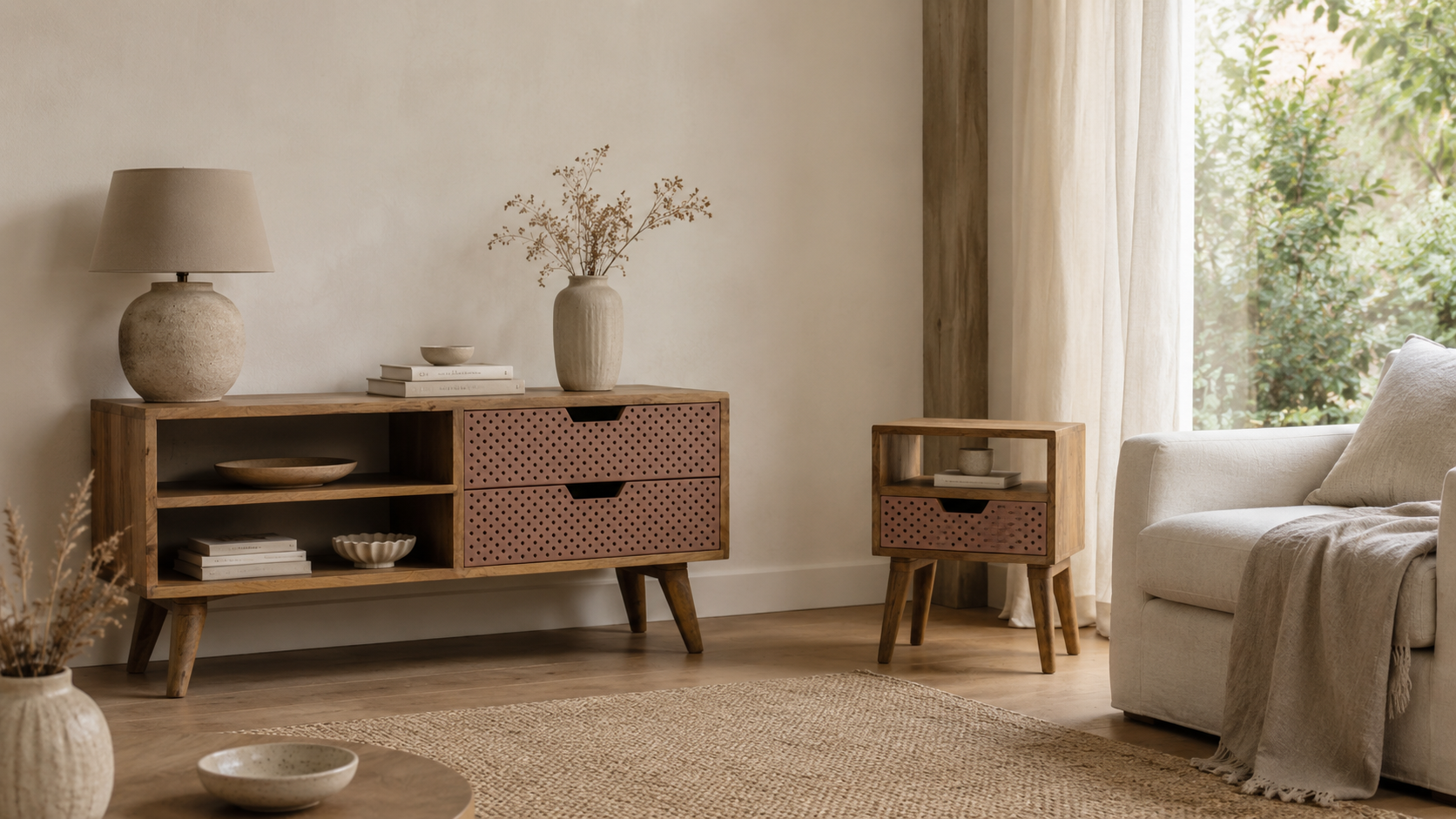 Calm neutral living room with a wooden media unit and matching side table, terracotta perforated drawers, cream sofa, ceramic lamp, dried stems, woven rug and soft natural light.